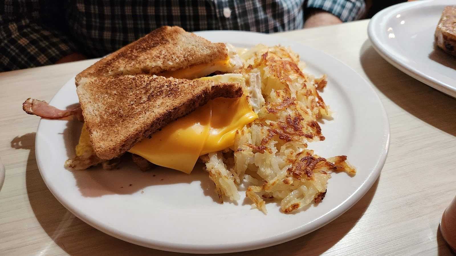 Grilled cheese sandwich and hash browns on a white plate, served on a wooden table.