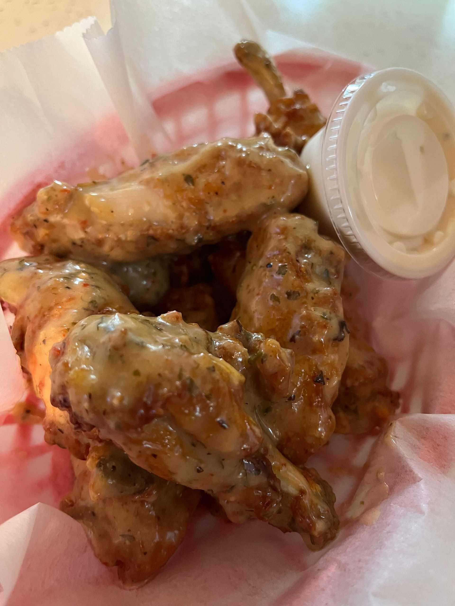 Chicken wings covered in creamy sauce served with a side of dipping sauce in a basket.