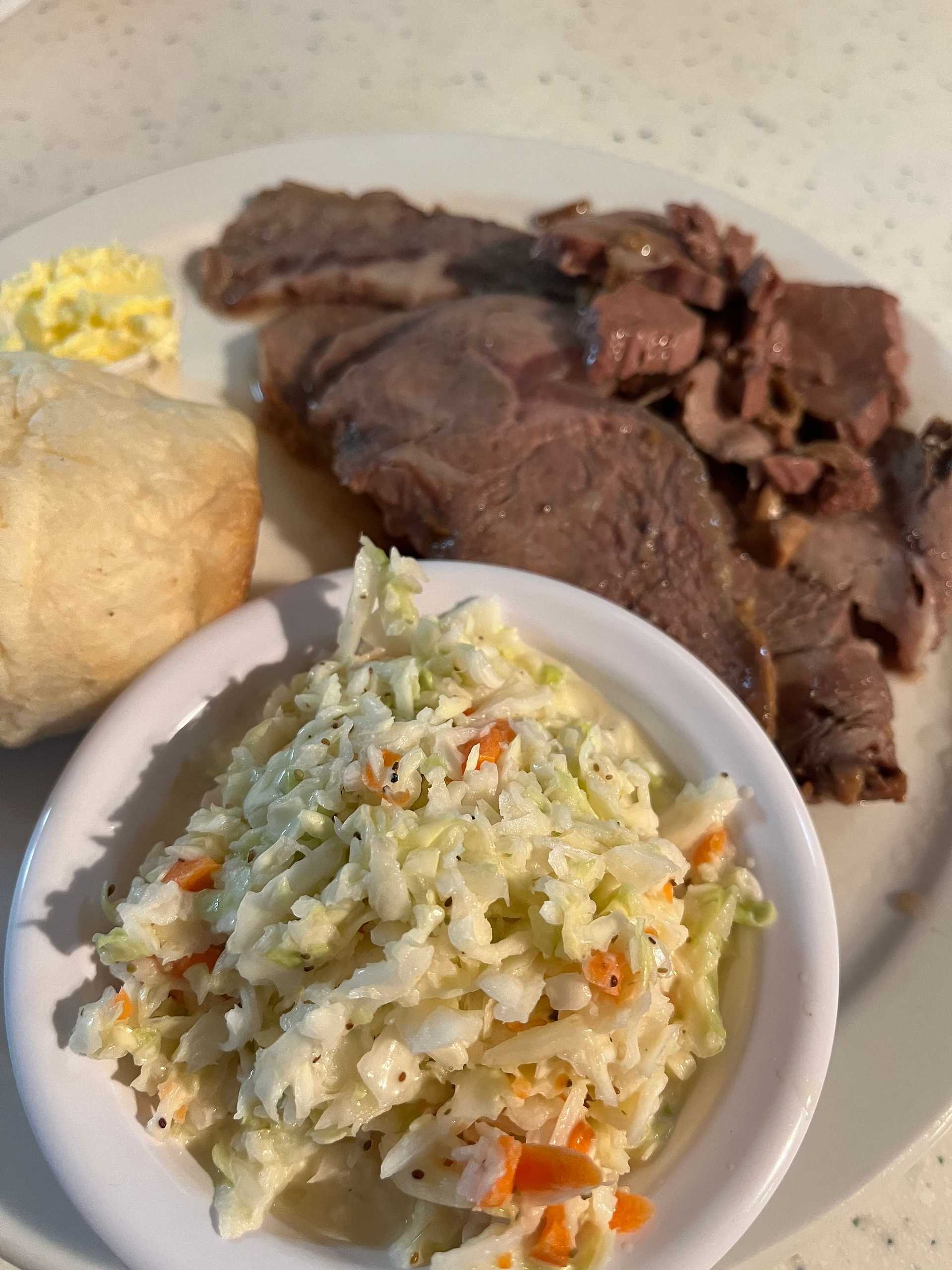 Plate of roast beef slices with coleslaw, dinner roll, and a small portion of butter.