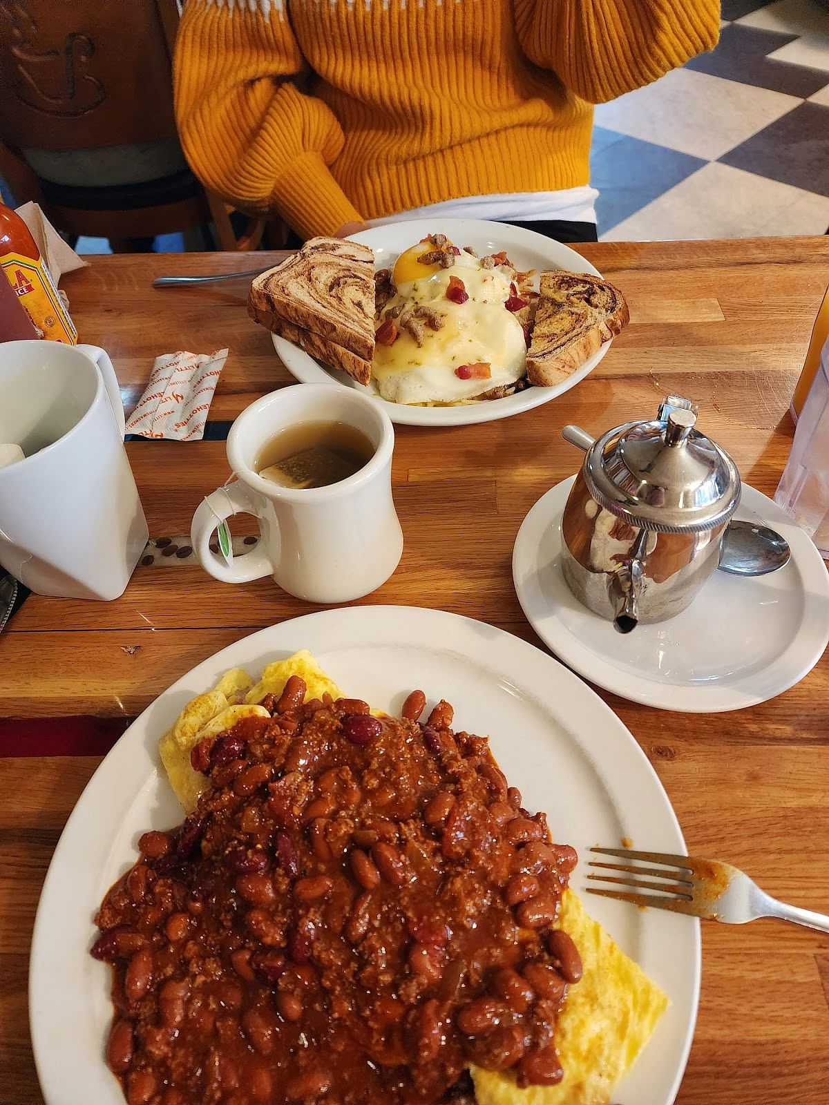 Plates of breakfast food on a wooden table, including chili omelet, coffee, and French toast.