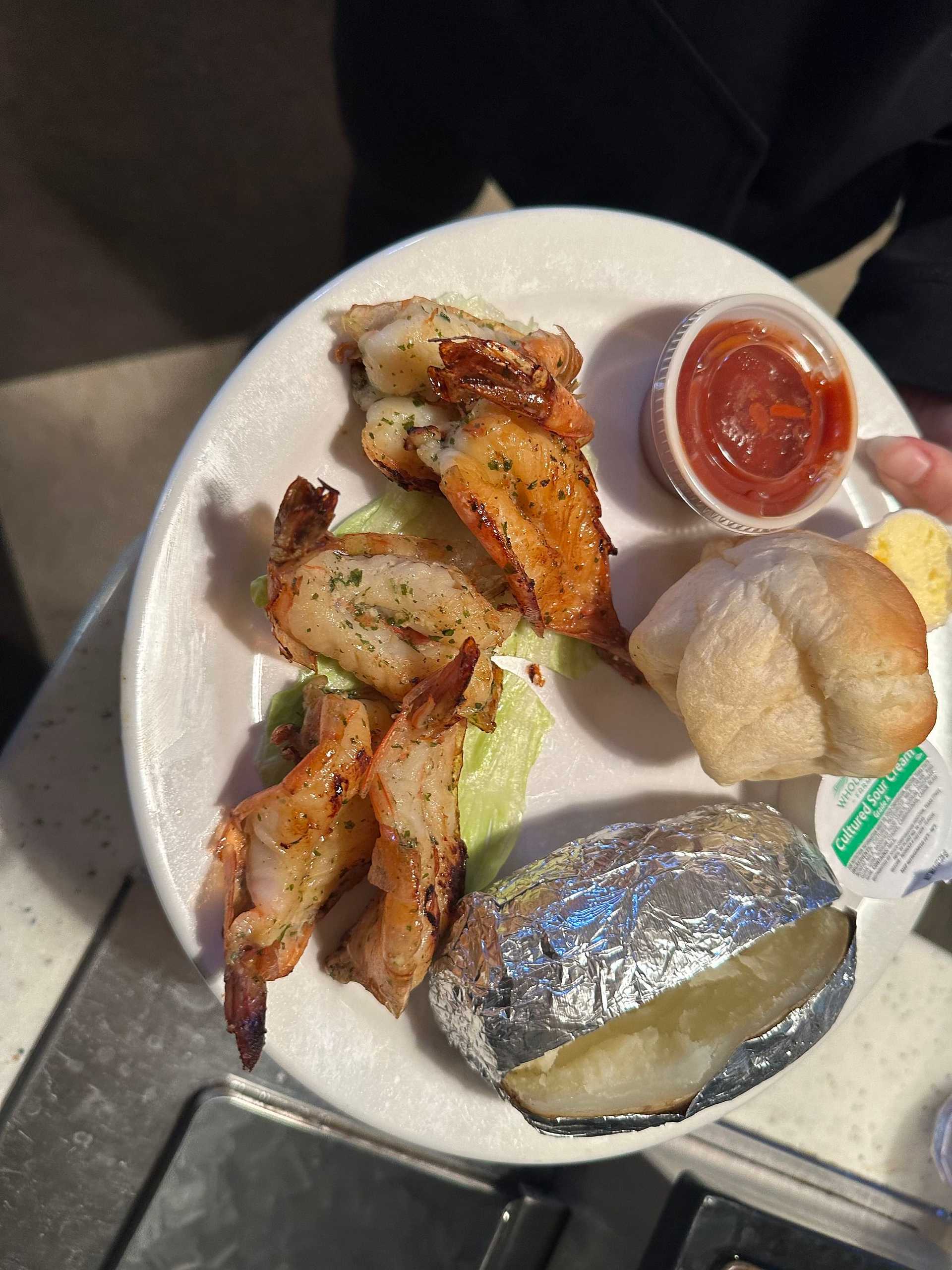 Plate with grilled shrimp, baked potato, roll, lettuce garnish, and cocktail sauce.