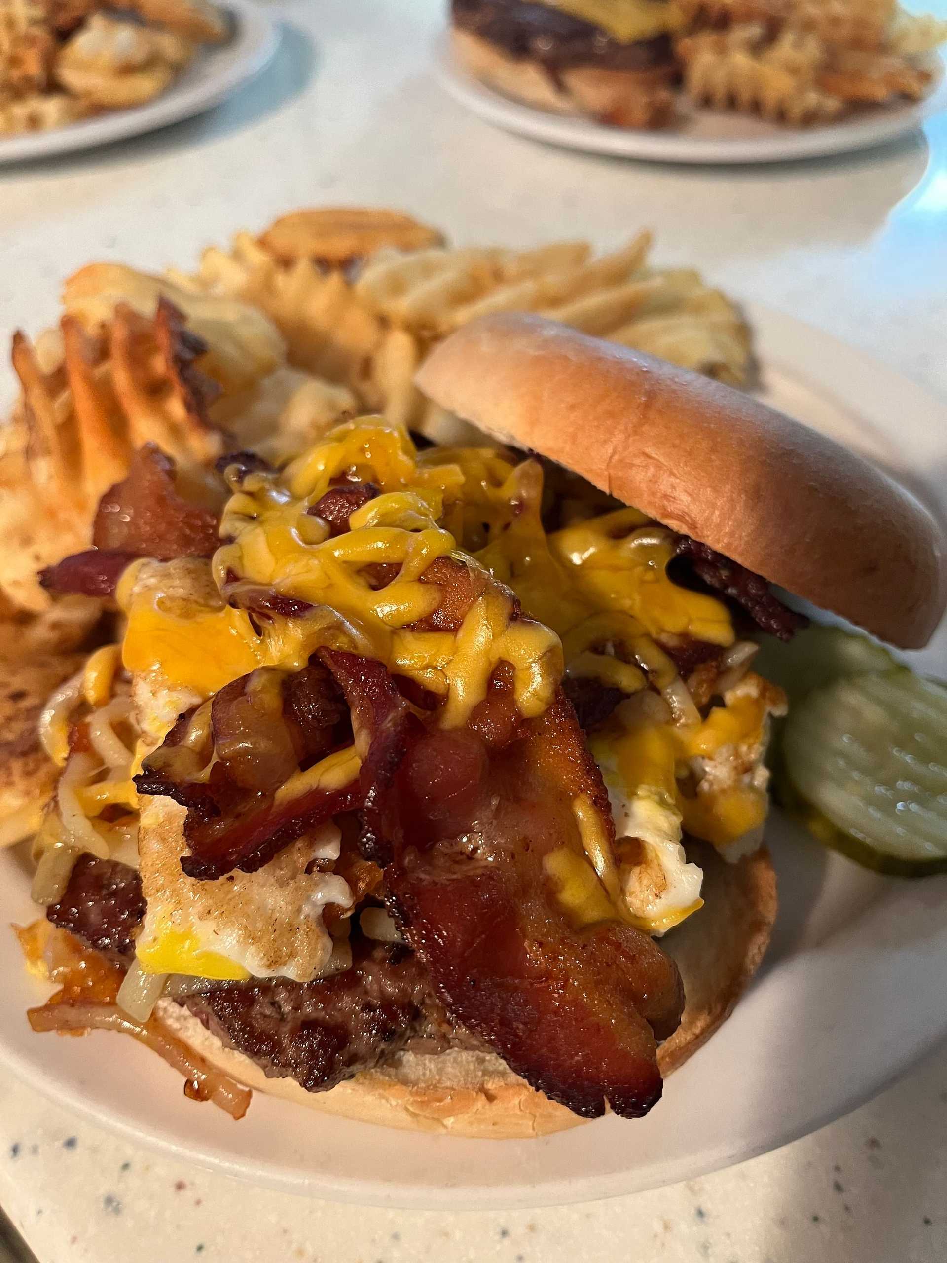 Cheeseburger topped with bacon and cheddar, served with waffle fries and pickle slices.